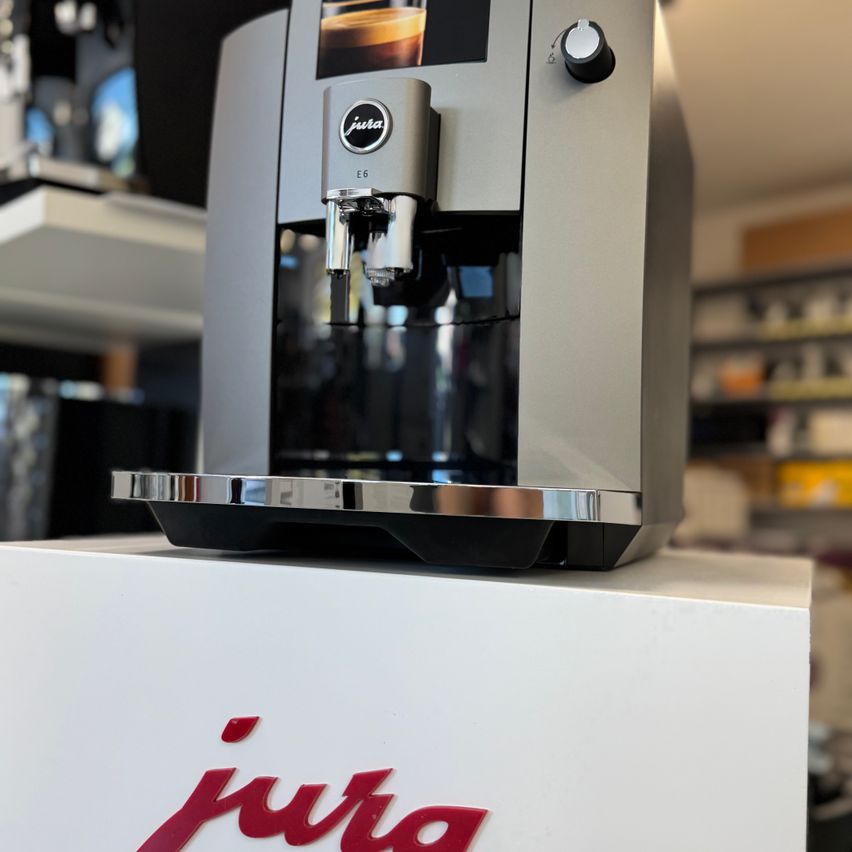 Eine Jura E6 Espressomaschine ist auf einem weißen Podest mit ihrem Logo im Vordergrund ausgestellt.