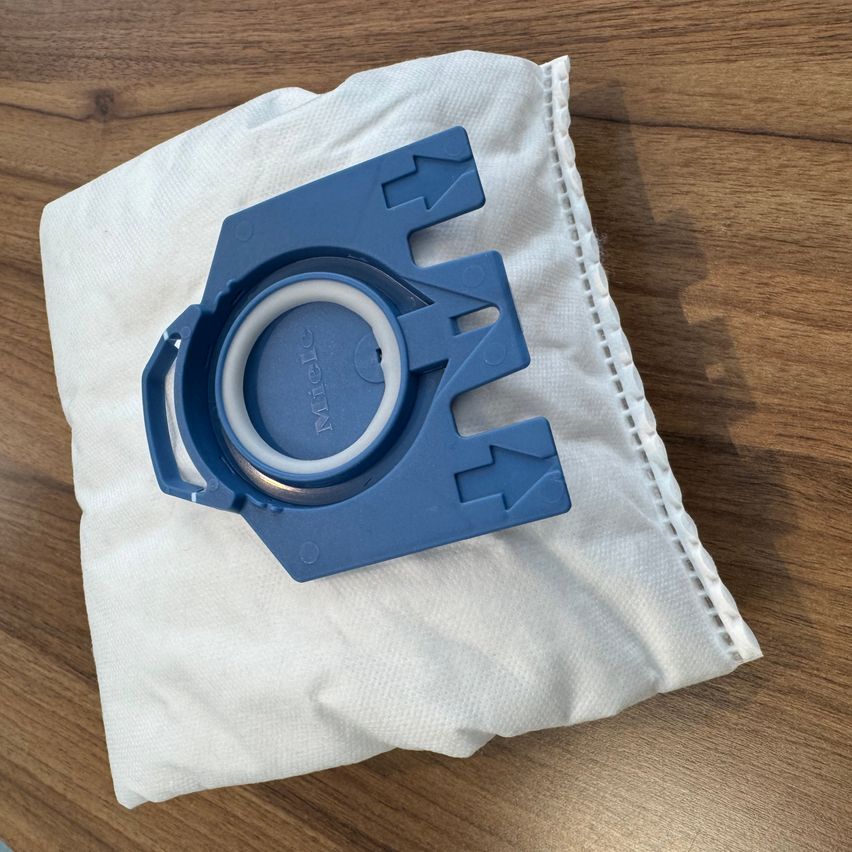 A blue plastic container sits on a folded white cloth on a wooden surface. The container has a white lid and a blue label.