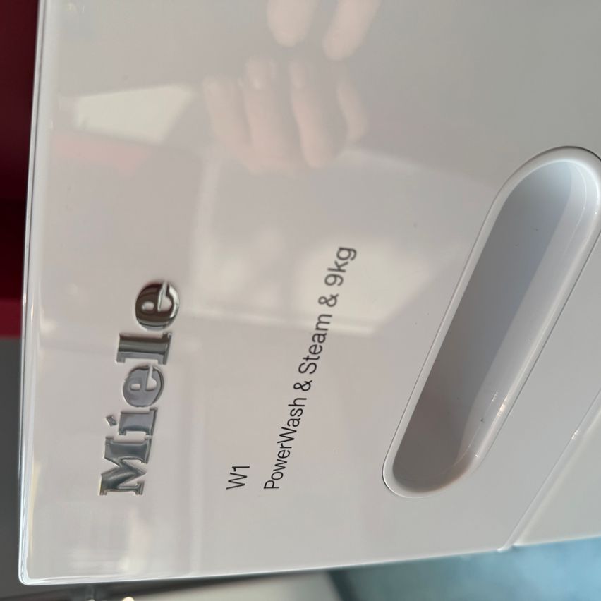 Ein weißes Gerät mit 'Miele'-Marke und 'PowerWash & Steam & 9kg'-Text. Es handelt sich wahrscheinlich um eine Waschmaschine.
