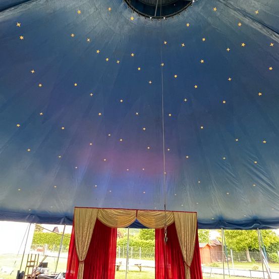 Ein Zelt mit blauer Decke und roten Vorhängen. Die Decke hat gelbe Sterne. Das Zelt steht auf einem Rasenfeld.