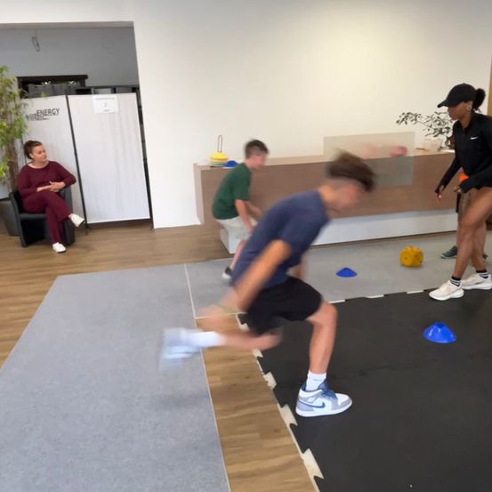 Drei Personen sind in einem Fitnessstudio und machen Übungen. Eine Person läuft. Zwei Personen stehen. Eine Frau sitzt auf einem Stuhl.