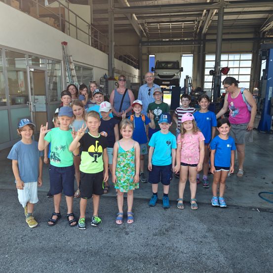 Eine Gruppe von Kindern und Erwachsenen posiert für ein Foto in einer Garage, wobei zwei Erwachsene im Hintergrund stehen.