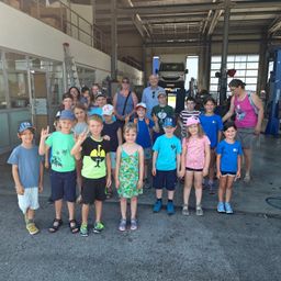 Eine Gruppe von Kindern und Erwachsenen posiert für ein Foto in einer Garage, wobei zwei Erwachsene im Hintergrund stehen.