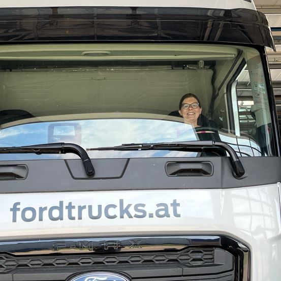 Eine Frau sitzt auf dem Fahrersitz eines weißen Ford-Lkws mit dem Wort 'fordtrucks.at' auf der Vorderseite.