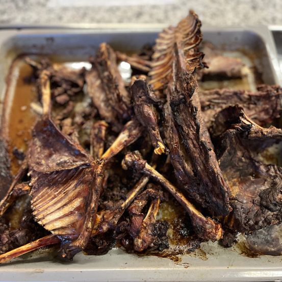 Ein Tablett mit gekochtem Fleisch mit Knochen, einschließlich Rippen, und etwas Fleisch auf der Seite. Das Fleisch ist gebräunt und scheint gut gekocht zu sein.