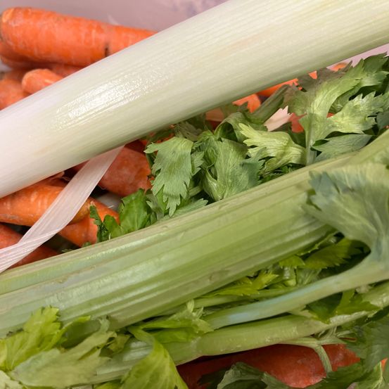 Ein Nahaufnahme von Gemüse. Es gibt Selleriestangen, grüne Blätter und Karotten. Die Karotten sind orange.