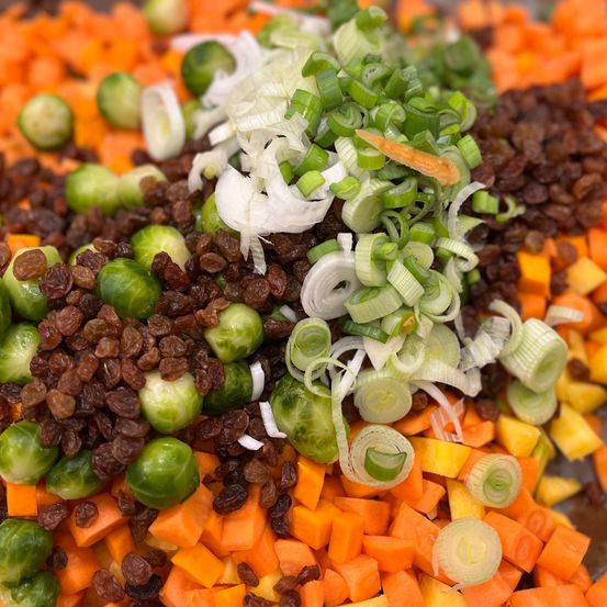 Ein Nahaufnahme von verschiedenen gehackten Gemüsesorten, darunter Karotten, Rosenkohl und Rosinen. Die Gemüsesorten sind so angeordnet, dass sie einem Haufen ähneln.