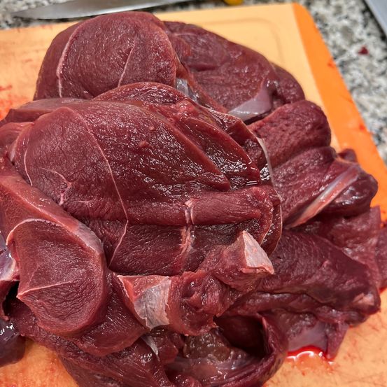 Eine Nahaufnahme von rohen Rindfleischstücken auf einem orangefarbenen Schneidebrett. Das Fleisch ist dunkelrot und scheint frisch geschnitten zu sein.