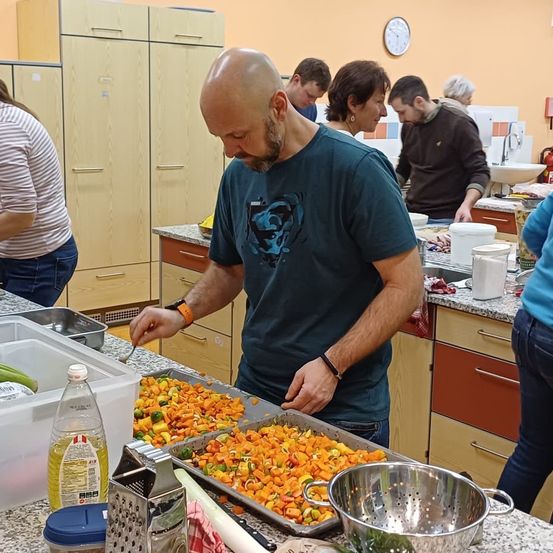 Ein Mann in einer Küche, der Gemüse auf einem Tresen zubereitet, mit anderen dahinter.