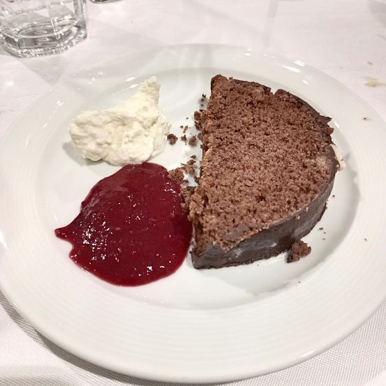 Ein weißer Teller mit einem Stück Schokoladenkuchen, einer Kugel weißer Sahne und einer roten Beerensauce. Der Kuchen ist dunkelbraun, die Sahne hell. Die Sauce ist dick und lebhaft.