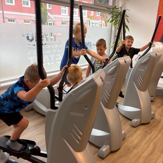 Fünf junge Jungen nutzen Laufbänder in einem Fitnessstudio, wobei ein Junge in einem blauen Shirt die Gruppe anführt.