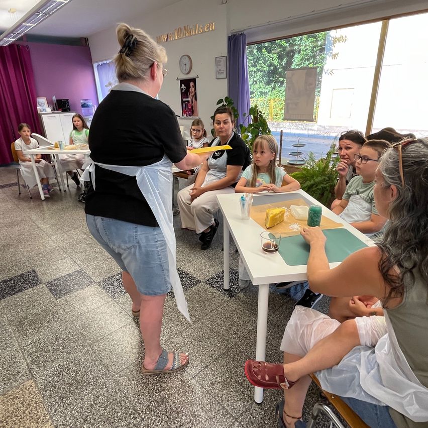 Eine Gruppe von Kindern sitzt an einem Tisch, wobei eine erwachsene Frau ihnen beibringt, wie man Käse herstellt.