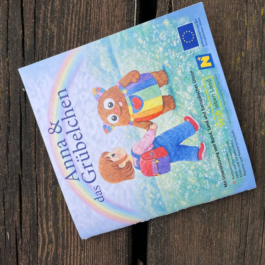 A children's book with a colorful illustration of a girl and bear with a rainbow. The cover reads Anna and Grubeln, das Grüble.