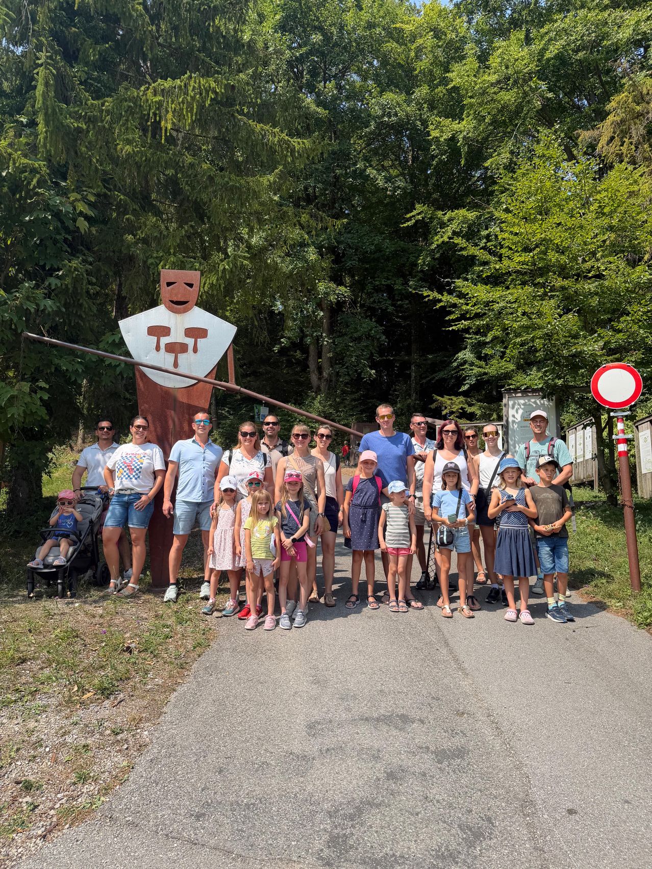 Eine Gruppe von Menschen, einschließlich Erwachsener und Kindern, posiert für ein Foto vor einer großen Holzstatue in einer Waldumgebung.