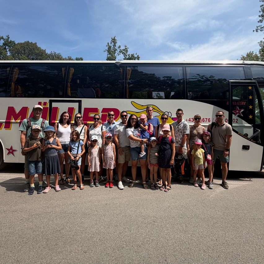 Eine Gruppe von Menschen, einschließlich Erwachsener und Kindern, steht vor einem Bus mit einem gelben Kater und einem roten Stern auf der Seite.