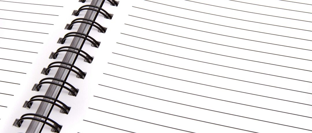 Nahaufnahme eines spiralgebundenen Notizbuchs mit weißem Einband, schwarzer Spiralbindung und linierten Seiten. Das Notizbuch ist geöffnet und zeigt leere Seiten zum Schreiben.