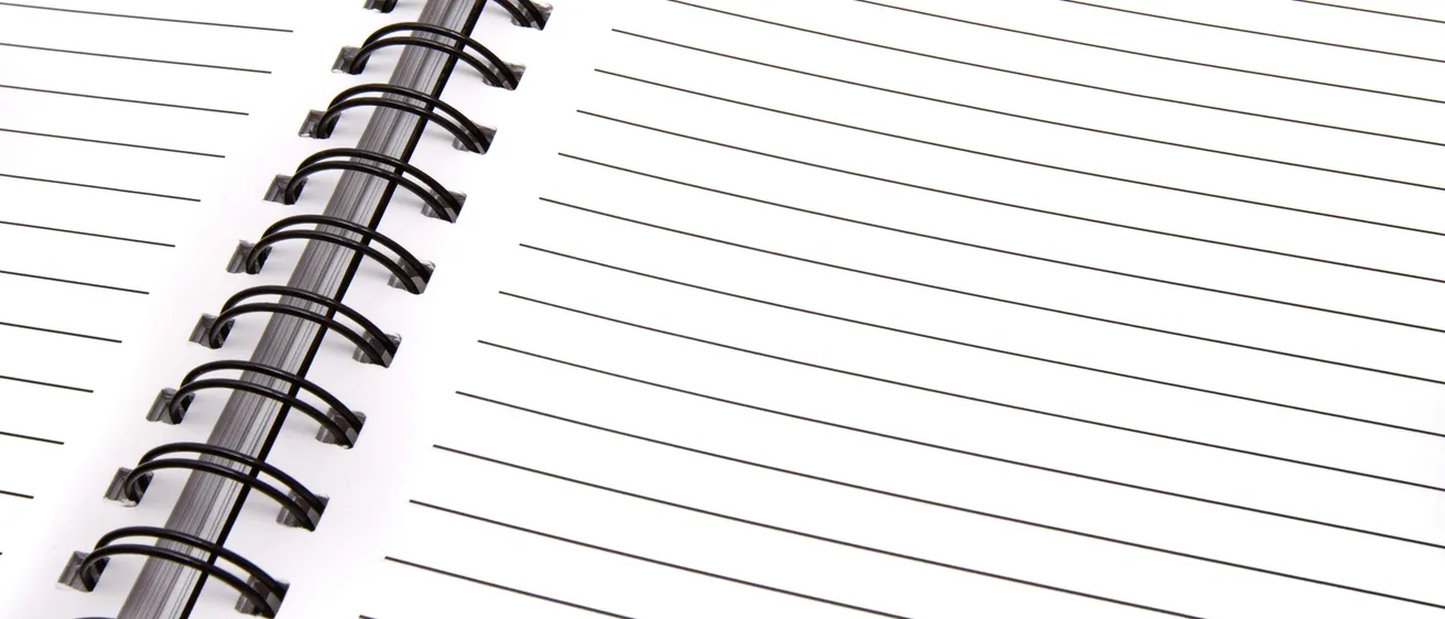 Nahaufnahme eines spiralgebundenen Notizbuchs mit weißem Einband, schwarzer Spiralbindung und linierten Seiten. Das Notizbuch ist geöffnet und zeigt leere Seiten zum Schreiben.