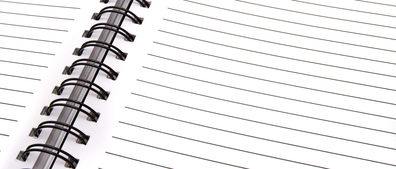 Nahaufnahme eines spiralgebundenen Notizbuchs mit weißem Einband, schwarzer Spiralbindung und linierten Seiten. Das Notizbuch ist geöffnet und zeigt leere Seiten zum Schreiben.