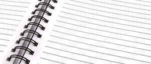 Nahaufnahme eines spiralgebundenen Notizbuchs mit weißem Einband, schwarzer Spiralbindung und linierten Seiten. Das Notizbuch ist geöffnet und zeigt leere Seiten zum Schreiben.