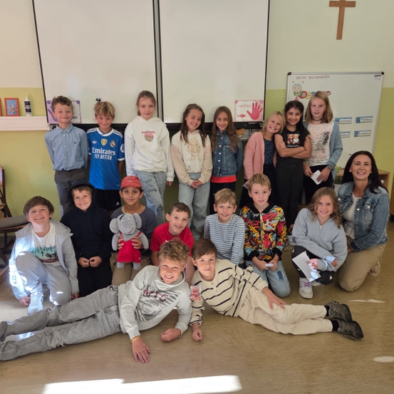Ein Klassenzimmer mit Kindern, einer Lehrerin und einem Kreuz an der Wand. Die Kinder posieren für ein Foto.