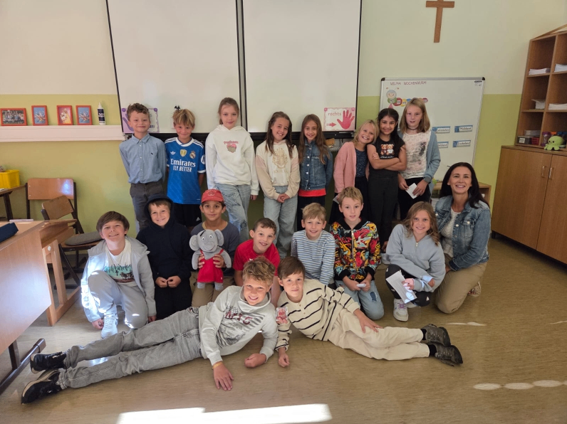 Ein Klassenzimmer mit Kindern, einer Lehrerin und einem Kreuz an der Wand. Die Kinder posieren für ein Foto.