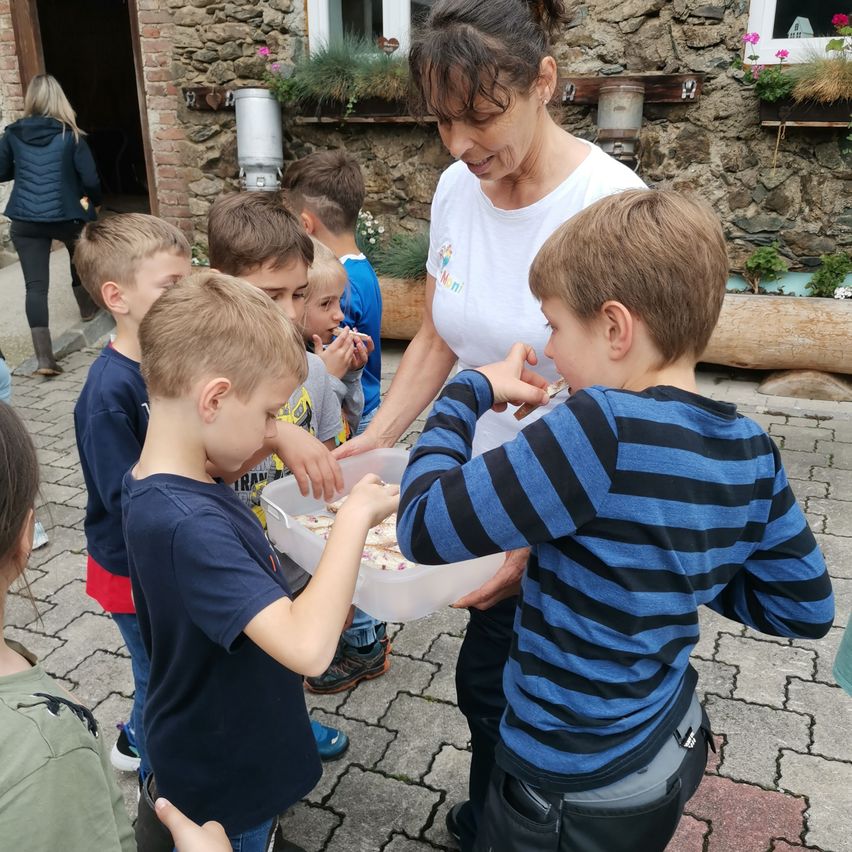 Eine Frau serviert Kindern in einer Reihe Essen und steht hinter einer Steinmauer mit Blumen.