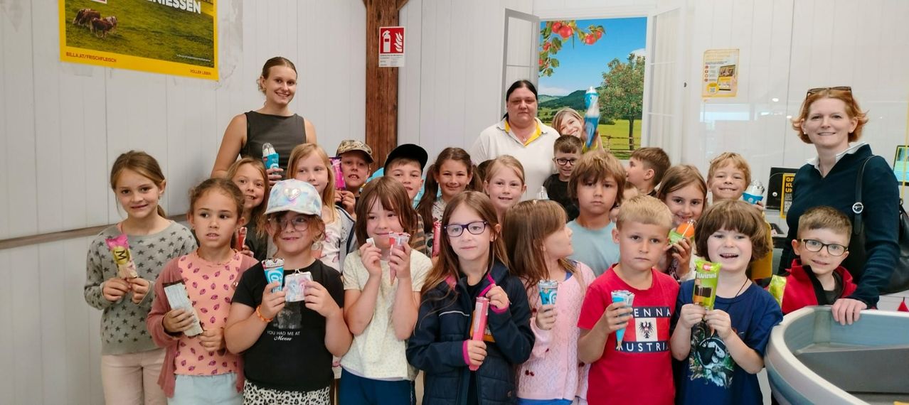 Eine Gruppe von Kindern und Erwachsenen in einem Raum, halten Zahnbürsten, einige mit Brille, eine Frau vorne, die ein Objekt hält.