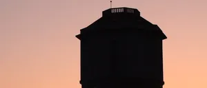 Die Silhouette eines Wasserturms steht vor einem Sonnenuntergangshimmel, mit Bäumen darunter sichtbar.
