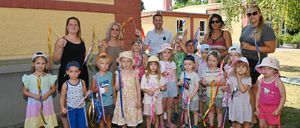 Eine Gruppe von Kindern und Erwachsenen mit bunten Bändern steht vor einem Gebäude.