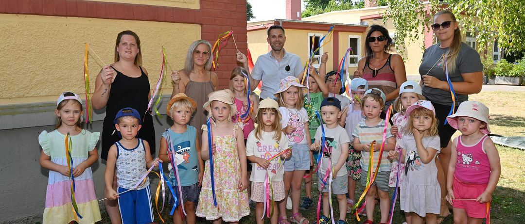 Eine Gruppe von Kindern und Erwachsenen mit bunten Bändern steht vor einem Gebäude.