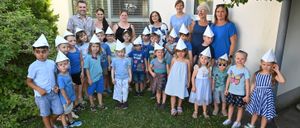 Eine große Gruppe von Kindern und Erwachsenen steht vor einem Gebäude und trägt Papierhüte. Die Kinder lächeln und einige haben Gesichtsbemalung. Die Erwachsenen stehen hinter den Kindern.