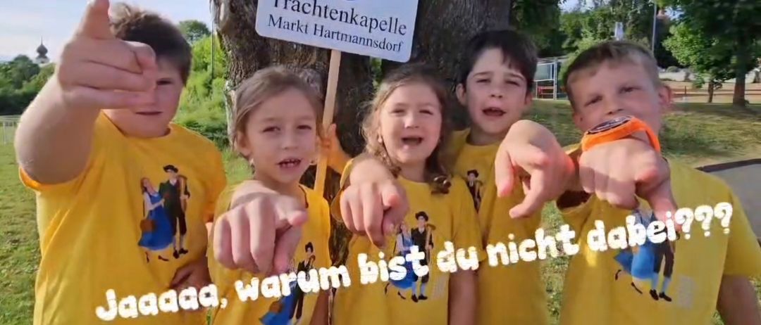 Fünf Kinder in gelben T-Shirts stehen neben einem Baum mit einem Schild. Sie scheinen für ein Foto zu posieren. Ein Kind gibt einen Daumen hoch.