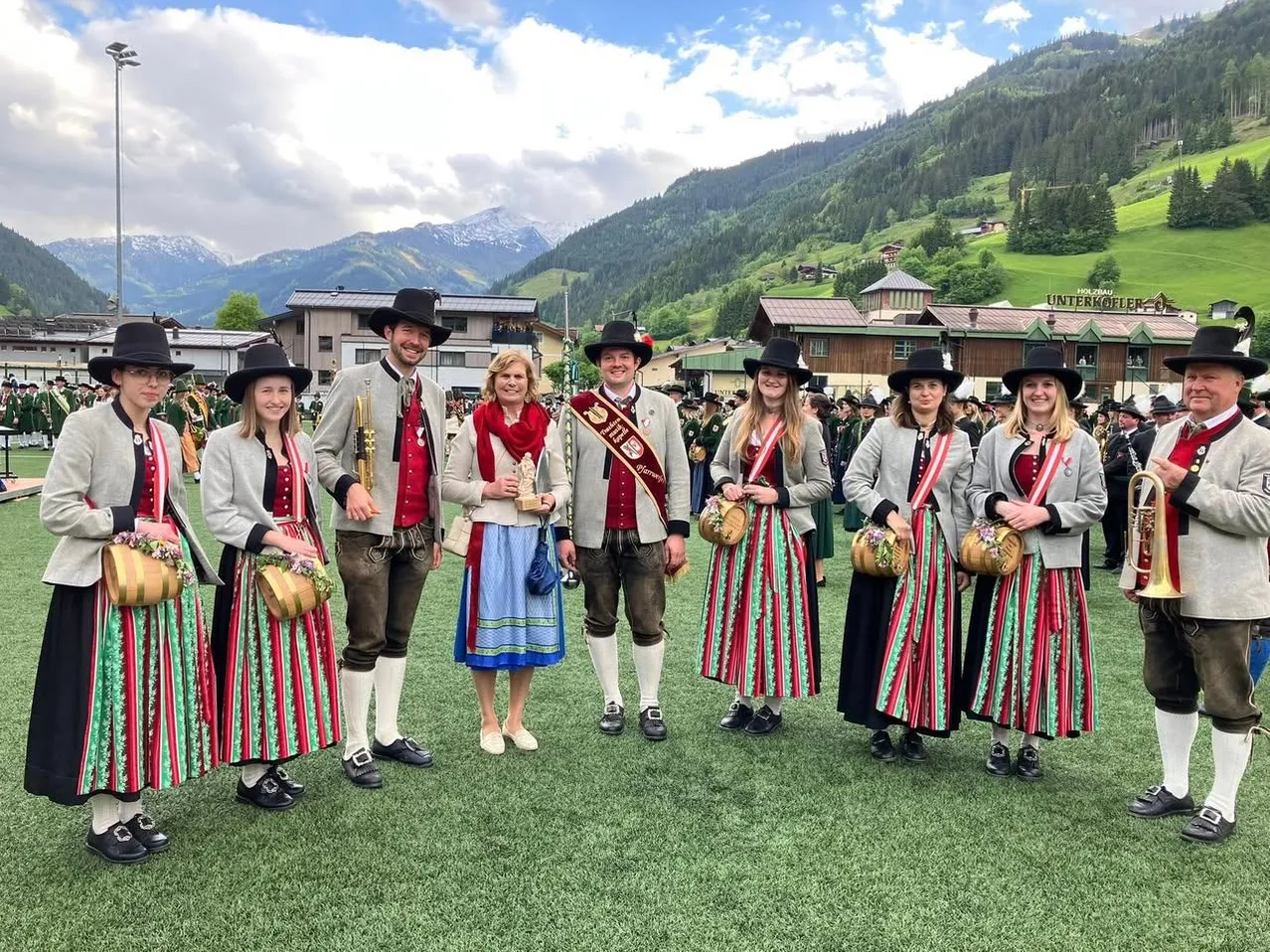 Eine Gruppe von Menschen in traditioneller Kleidung posiert für ein Foto auf einem grünen Feld mit Bergen im Hintergrund.