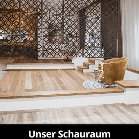 Innenansicht eines modernen Ausstellungsraums mit Holzböden, einem beigen Sessel und einer dekorativen Wand mit komplizierten Mustern. Der Raum verfügt über eine Treppe mit weißen Stufen und einem Metallgeländer.