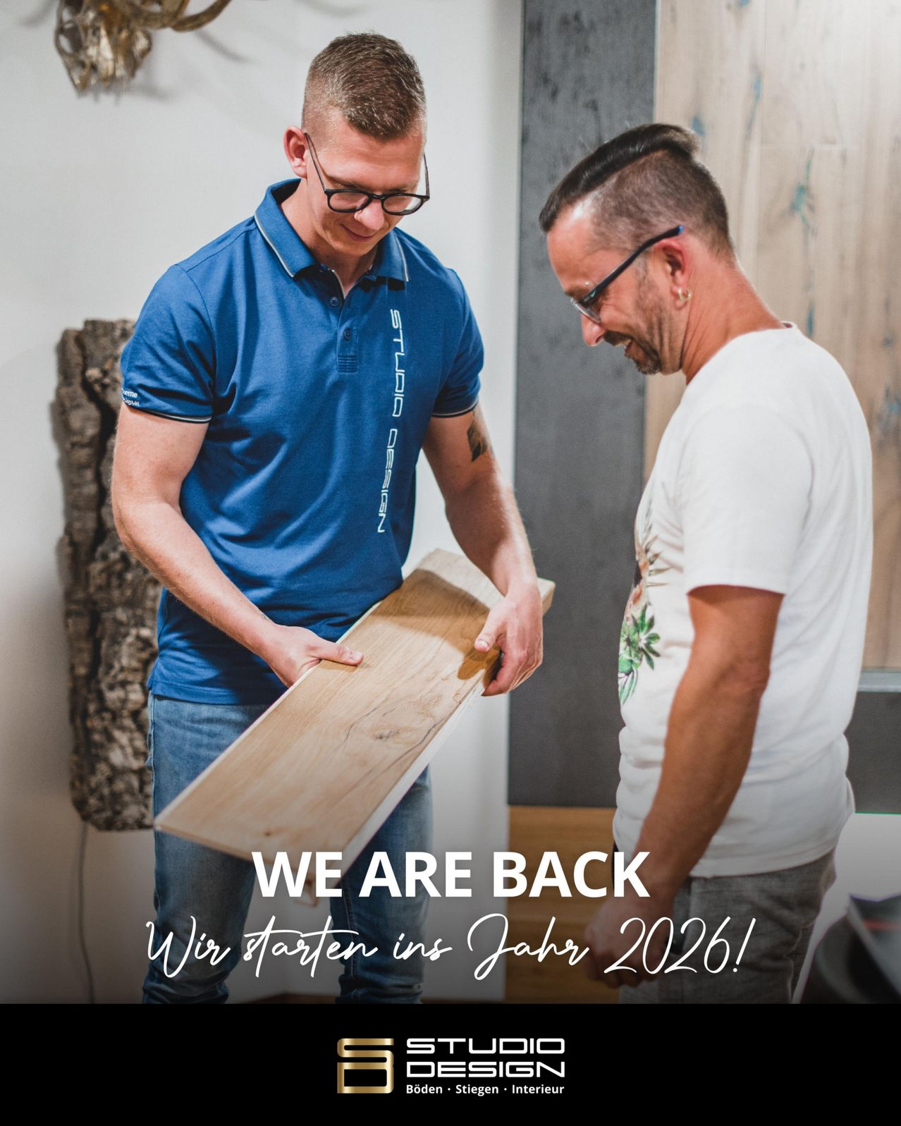 Zwei Männer sind drinnen, einer hält eine Holzplatte und lächelt, der andere schaut sie an. Beide tragen eine Brille. Ein Holzgerüst und der Text 'WIR STARTEN IM JAHR 2026!' sind im Hintergrund.