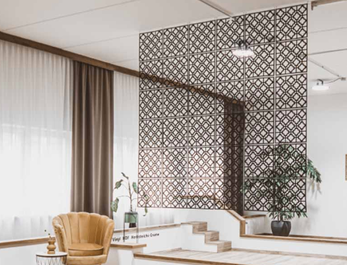 Ein modernes Zimmer mit gemusterter Wand und beigem Stuhl. Bepflanzte Pflanzen und Vorhänge sind auf beiden Seiten zu sehen. Eine Treppe führt in den oberen Stock.