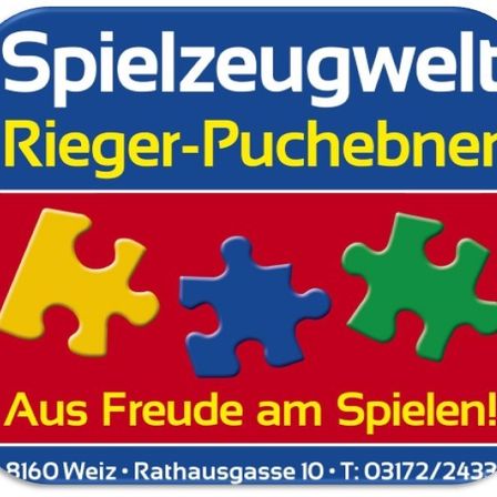 Ein blau-roter Schild mit weisser Schrift zeigt 'Spielzeugwelt Rieger-Puchebner', ein Puzzlestück-Logo und Kontaktdaten unten.