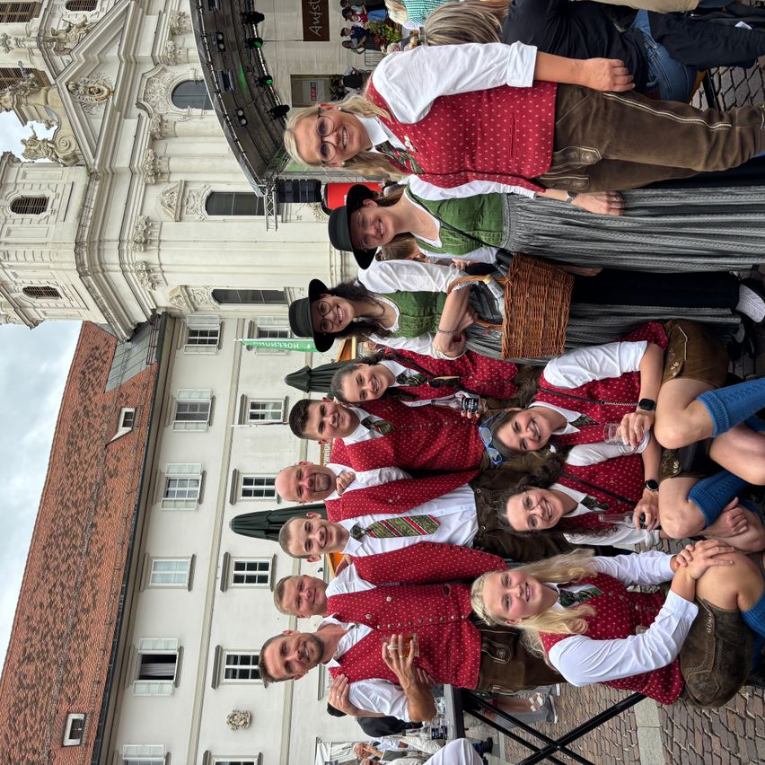 Eine Gruppe von Menschen in traditioneller Kleidung, möglicherweise für ein Festival, posiert für ein Foto vor einem historischen Gebäude.