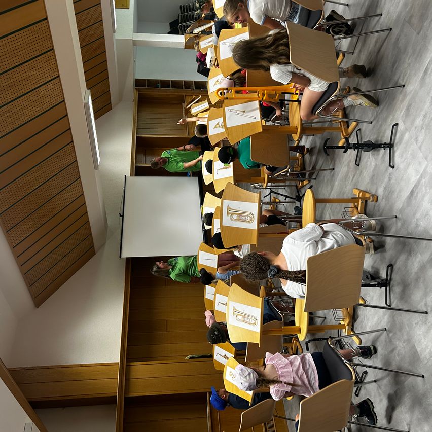 Eine Gruppe von Schülern sitzt in einem Klassenzimmer. Jeder Schüler hat eine Nummer auf seinem Schreibtisch. Ein Lehrer steht vor einer Tafel.