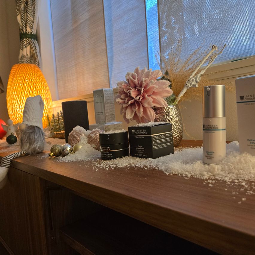 Ein Holztisch hat mehrere Schönheitsprodukte, darunter eine rosa Blume, eine silberne Lampe und eine Gnomfigur. Ein Vasen, ein Lautsprecher und eine Schachtel sind ebenfalls auf dem Tisch.