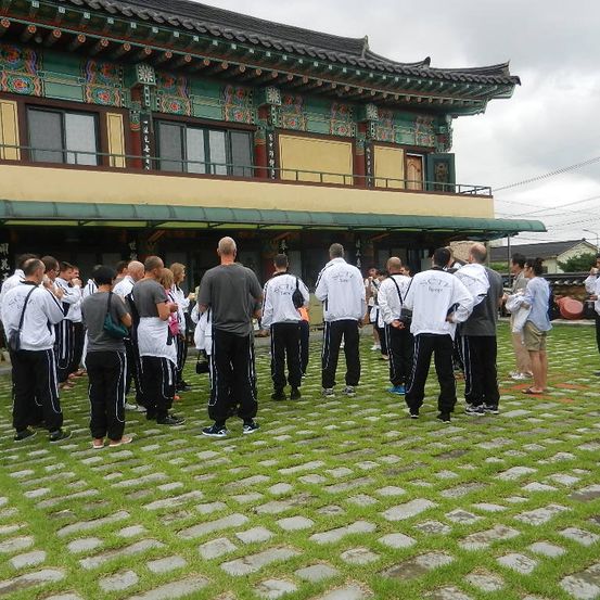 Gruppe von Personen in weißen Jacken und schwarzen Hosen, die vor einem traditionellen asiatischen Gebäude stehen.