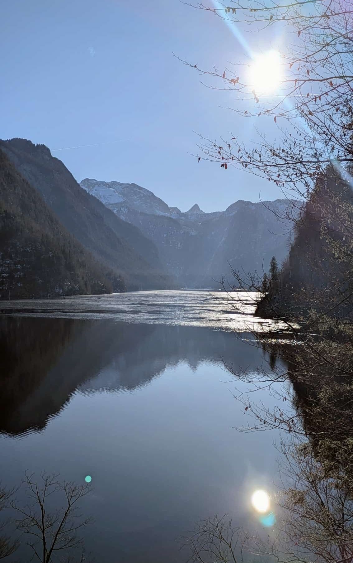 Ein ruhiger See eingebettet zwischen majestätischen Bergen, mit einem klaren blauen Himmel darüber und einigen Bäumen am Ufer.