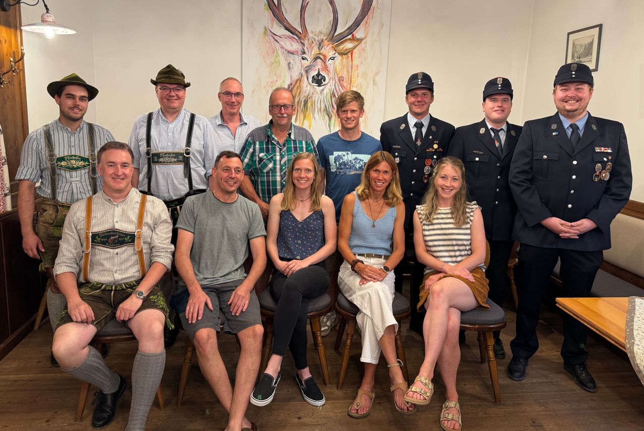 Eine Gruppe von Menschen, einschließlich Feuerwehrleute, posiert für ein Foto in einem Raum mit einem Hirschbild an der Wand.