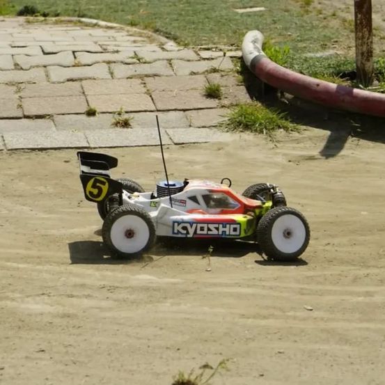 Ein ferngesteuertes Kyosho Rennauto mit der Nummer 5 auf einem unbefestigten Kurs.