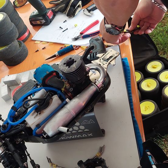 Eine Person arbeitet an einem mechanischen Projekt mit verschiedenen Werkzeugen auf einem Holztisch, einschließlich einer Bohrmaschine, Zangen und einem Schraubendreher. Das Projekt beinhaltet einen kleinen Motor mit Kabeln und anderen Komponenten.