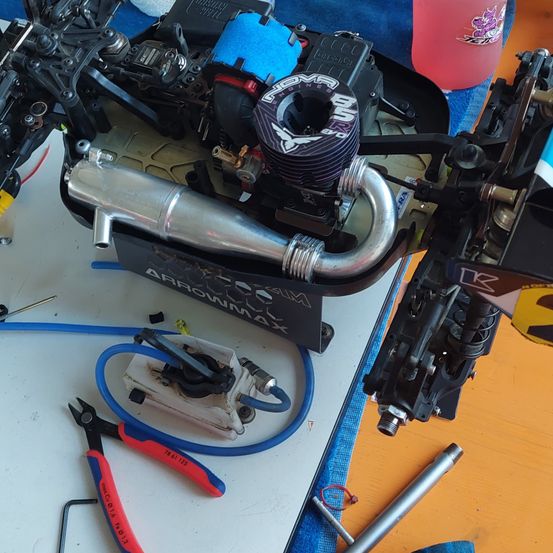 Ein zerlegter RC-Automotor auf einem weißen Tisch mit Werkzeugen und Kabeln. Eine rosa Flasche im Hintergrund.