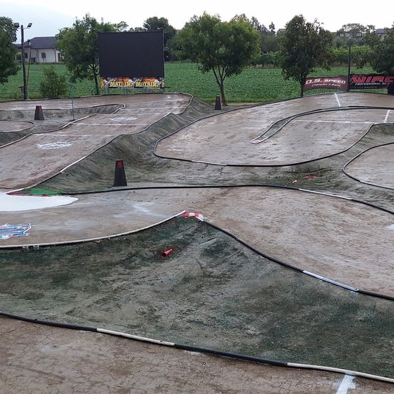 Eine Rennstrecke mit mehreren Kurven und Biegungen. Sie hat eine große schwarze Leinwand, Bäume und ein Gebäude im Hintergrund.