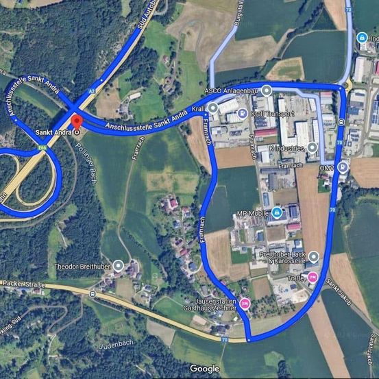 Eine Karte zeigt eine Luftaufnahme einer Route mit blauen Linien, die Straßen und Wege darstellen. Ein roter Punkt markiert einen bestimmten Ort, und verschiedene Wahrzeichen, Gebäude und Straßen sind beschriftet.