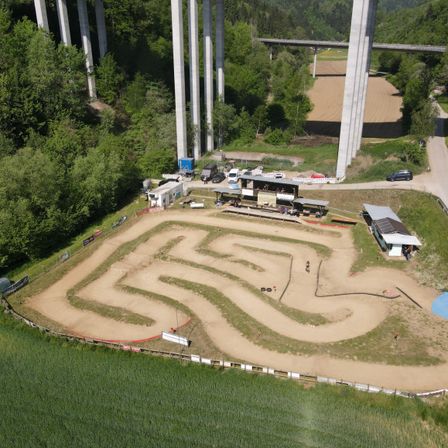 Luftaufnahme einer Erdstrecke mit einem labyrinthartigen Muster, in der Nähe einer Brücke, mit mehreren geparkten Fahrzeugen in der Nähe.