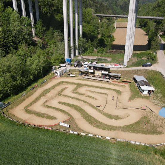 Luftaufnahme einer Erdstrecke mit einem labyrinthartigen Muster, in der Nähe einer Brücke, mit mehreren geparkten Fahrzeugen in der Nähe.